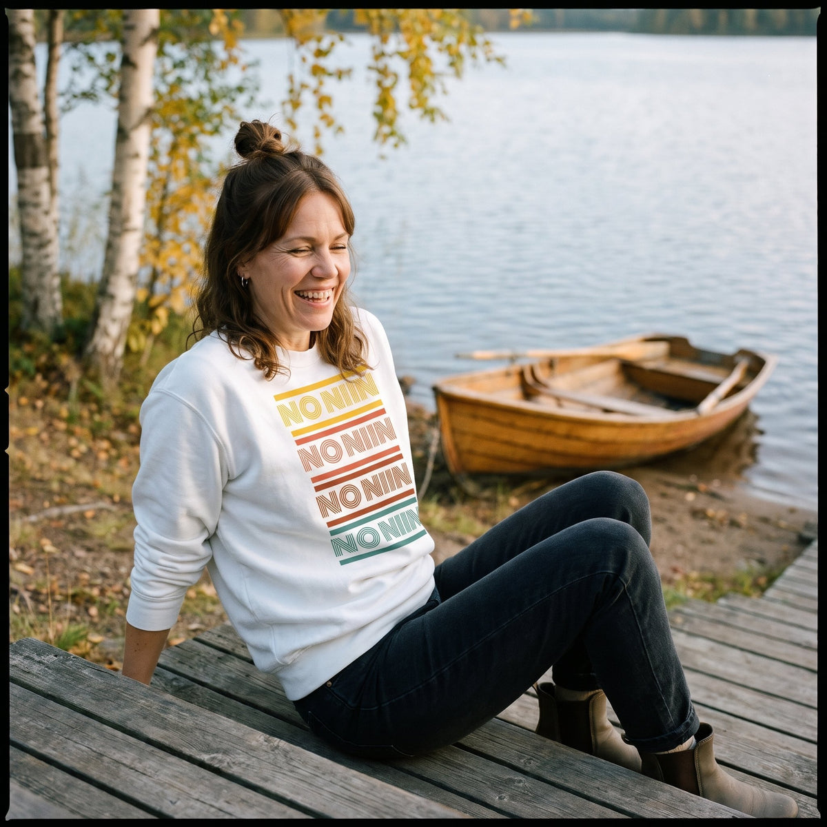 No niin retro sweatshirt in white, worn by a laughing woman sitting on wooden steps by a Finnish lake with a rowing boat, Very Finnish Problems