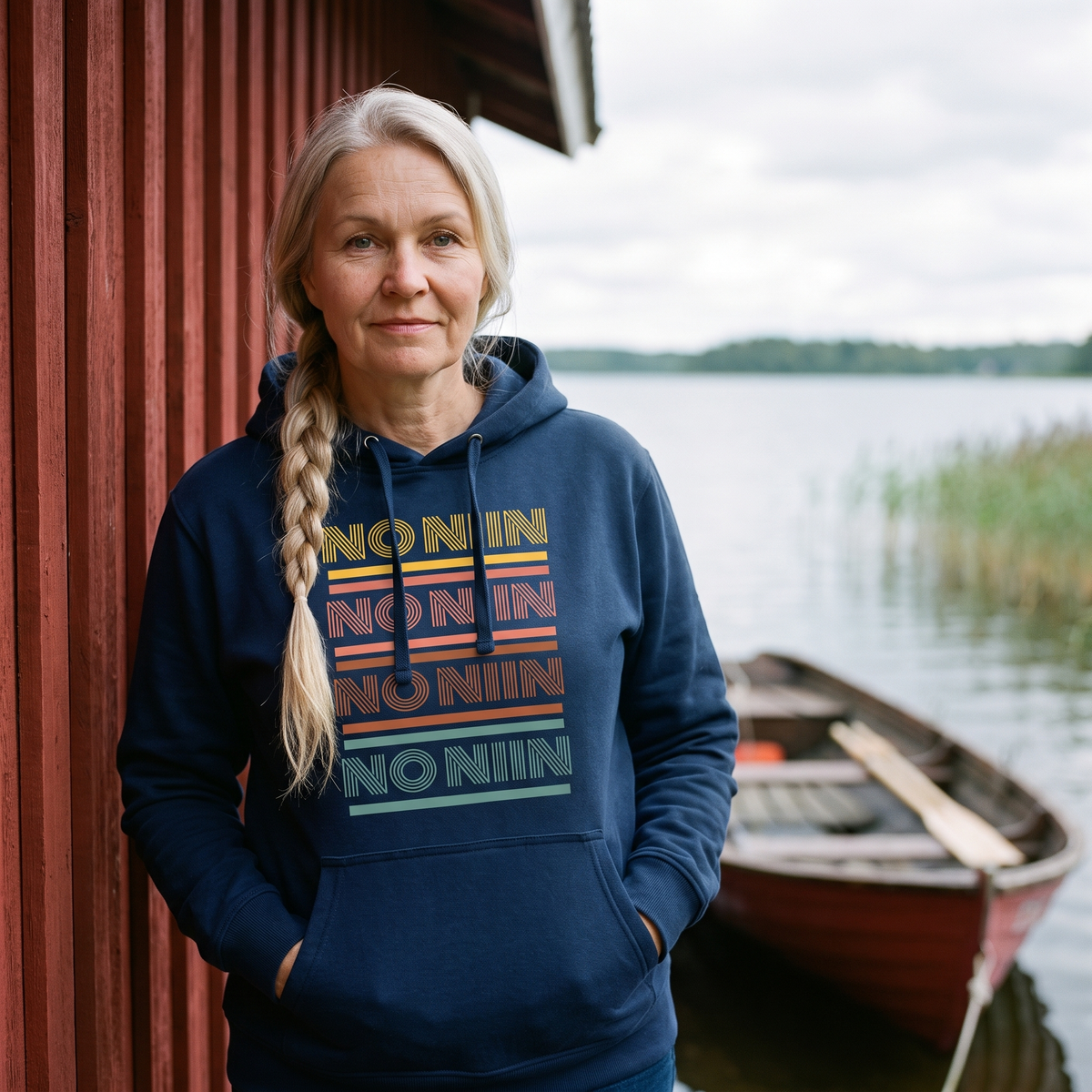 No niin retro Finnish language hoodie in navy, worn by Anneli beside a Finnish lakeside boathouse, Very Finnish Problems