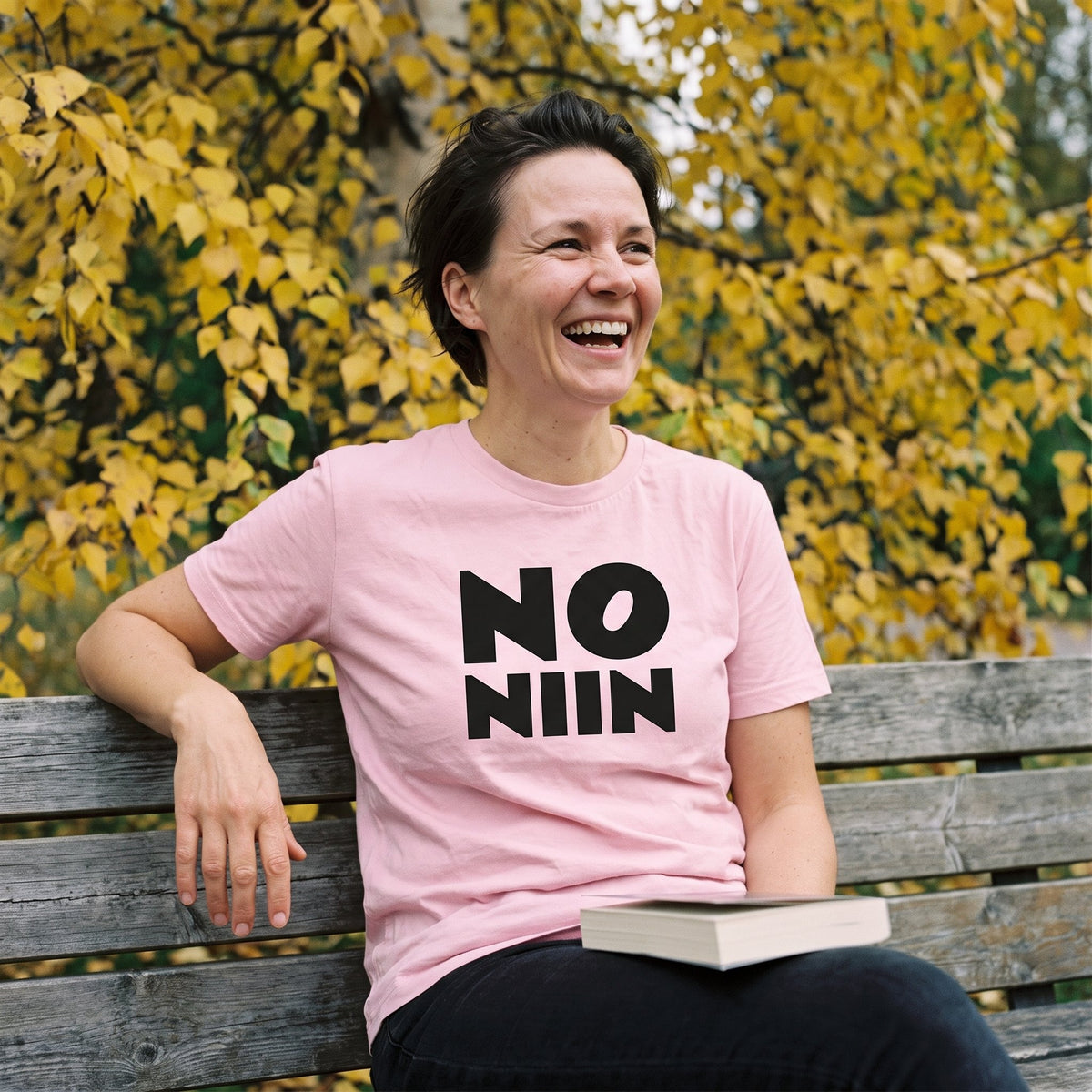 Katja wearing the pink No niin stacked t-shirt on a park bench, Very Finnish Problems
