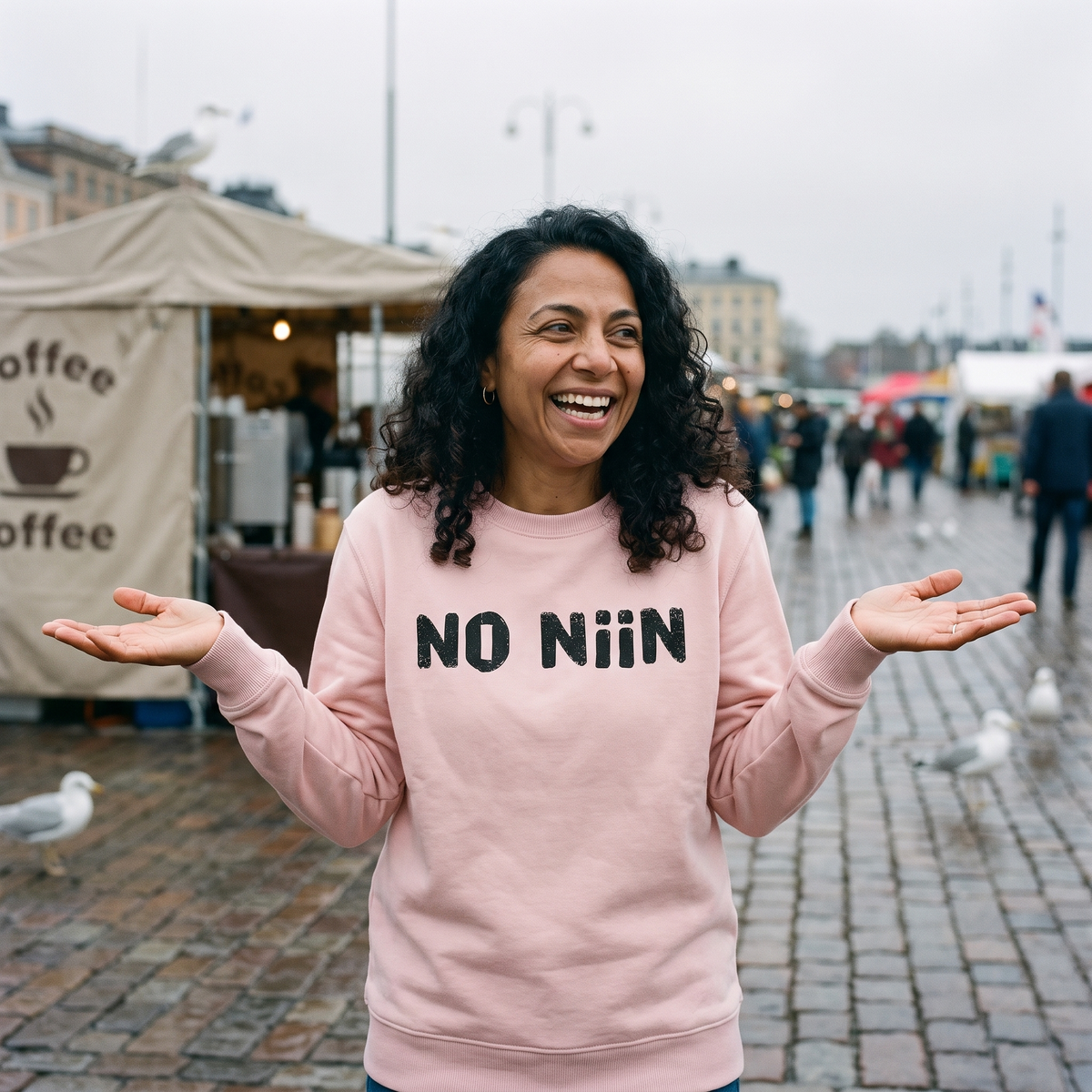 No niin Finnish language sweatshirt in light pink, worn by Nea shrugging in a Finnish market square, Very Finnish Problems