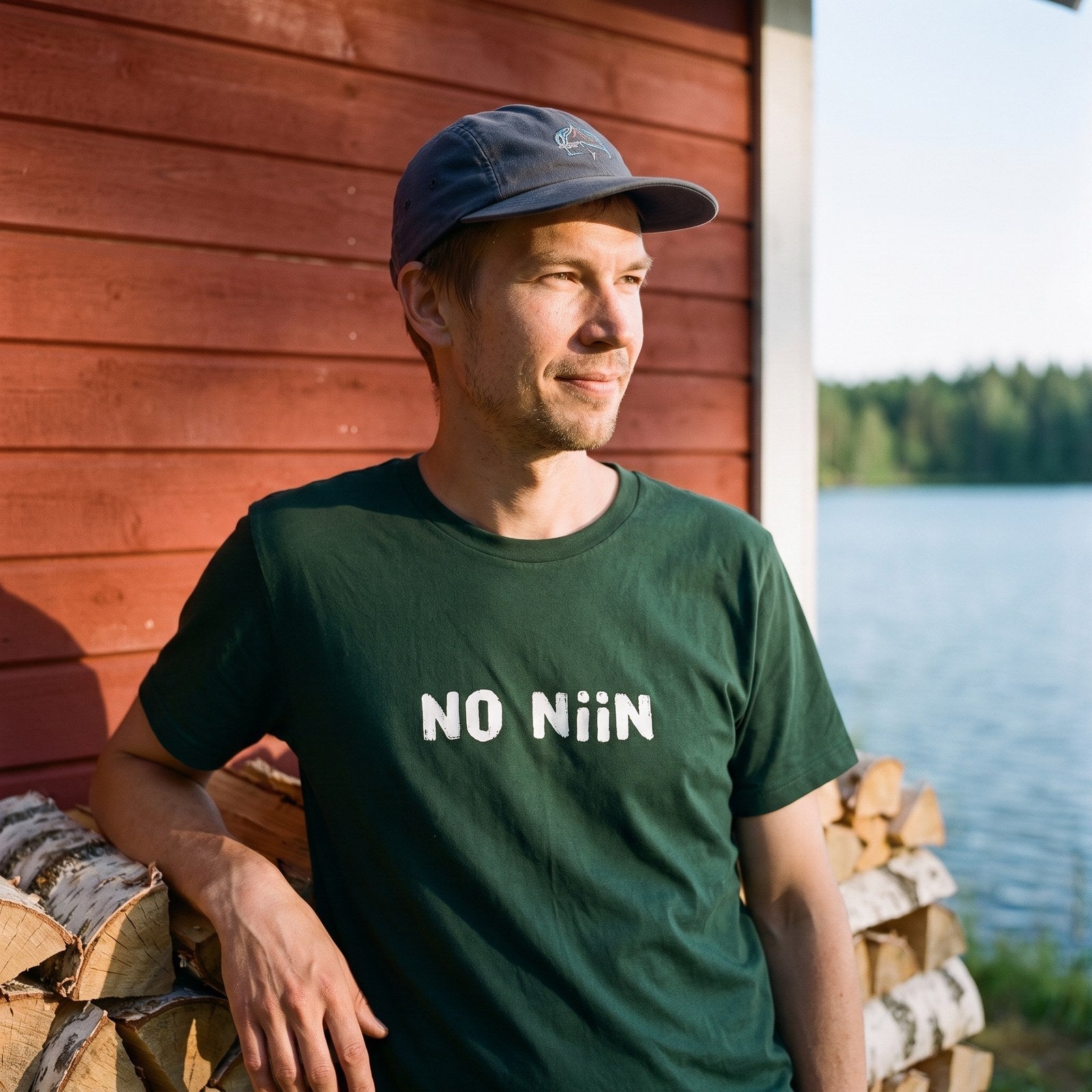 Man wearing the forest green No niin Finnish language t-shirt at a lakeside summer cottage, Very Finnish Problems