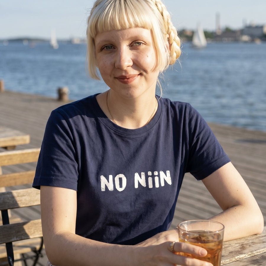 Woman wearing the navy No niin Finnish language t-shirt on a Helsinki seaside terrace, Very Finnish Problems