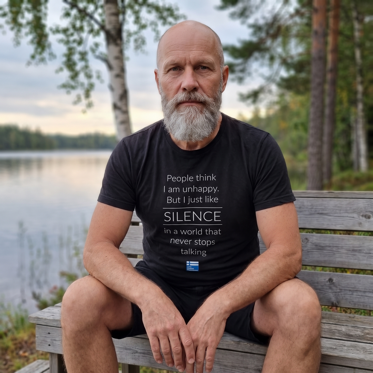 Not Unhappy Just Silent t-shirt in black, worn by Mikko on a lakeside bench, Very Finnish Problems