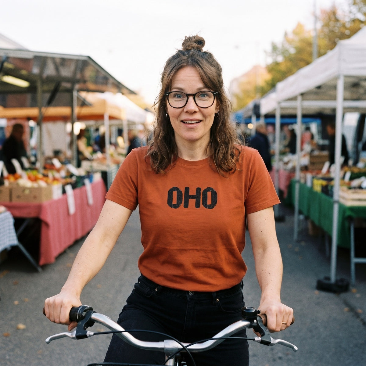 Oho Finnish language t-shirt in burnt orange, worn by a woman on her bike at a market square, Very Finnish Problems