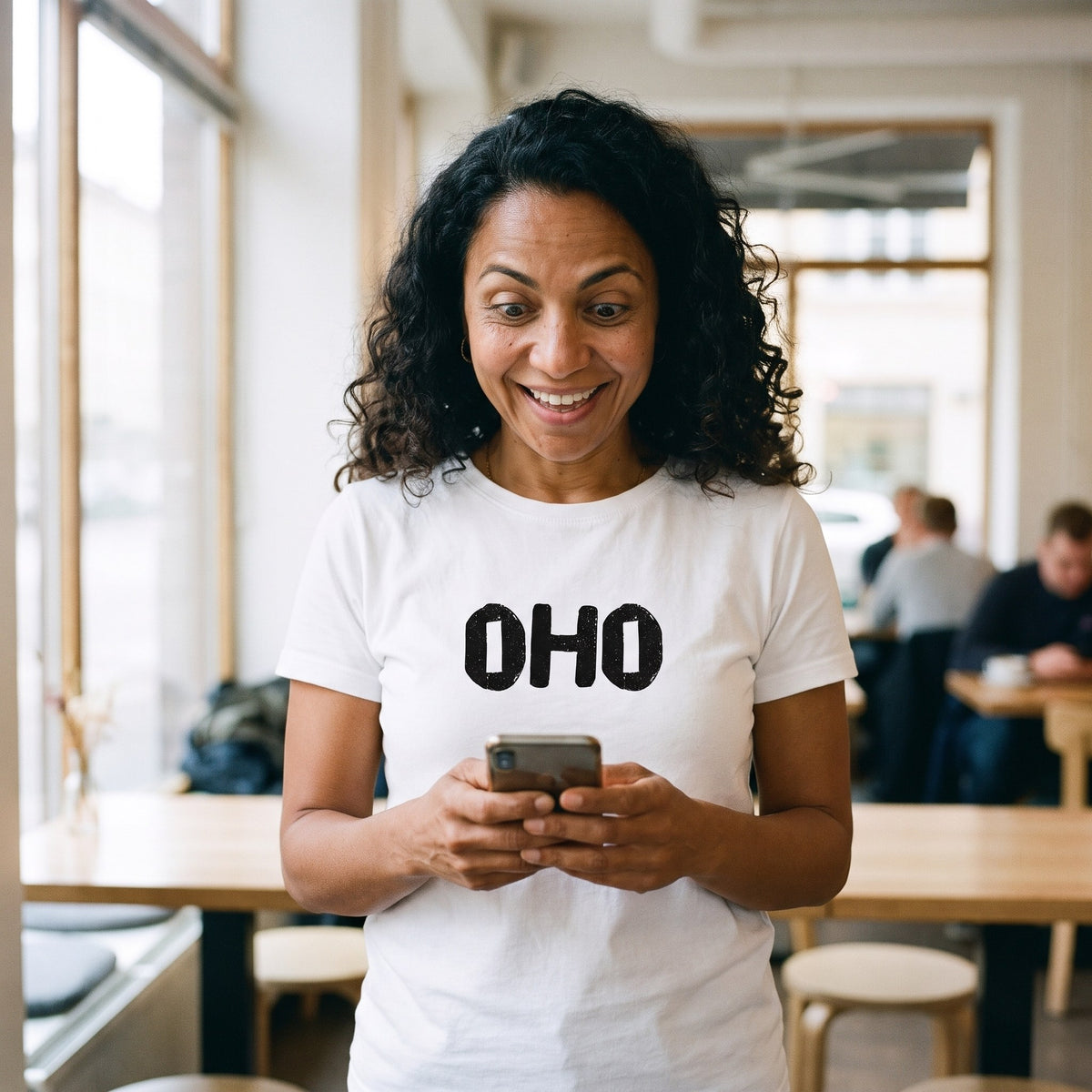 Oho Finnish language t-shirt in white, worn by a woman reading her phone wide-eyed in a café, Very Finnish Problems