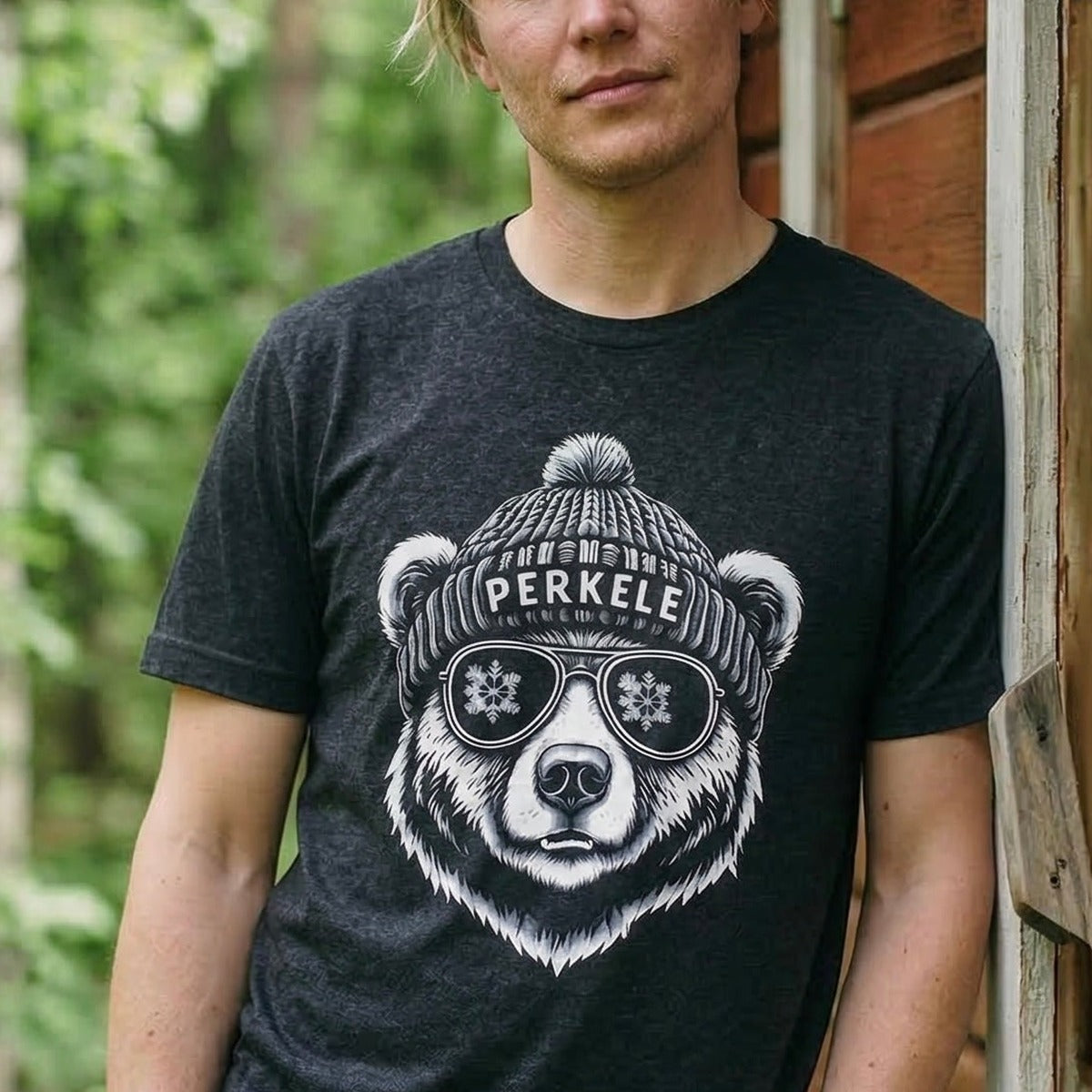 Man leaning on a Finnish cabin wearing the black heather Perkele Bear t-shirt, print close and legible, Very Finnish Problems