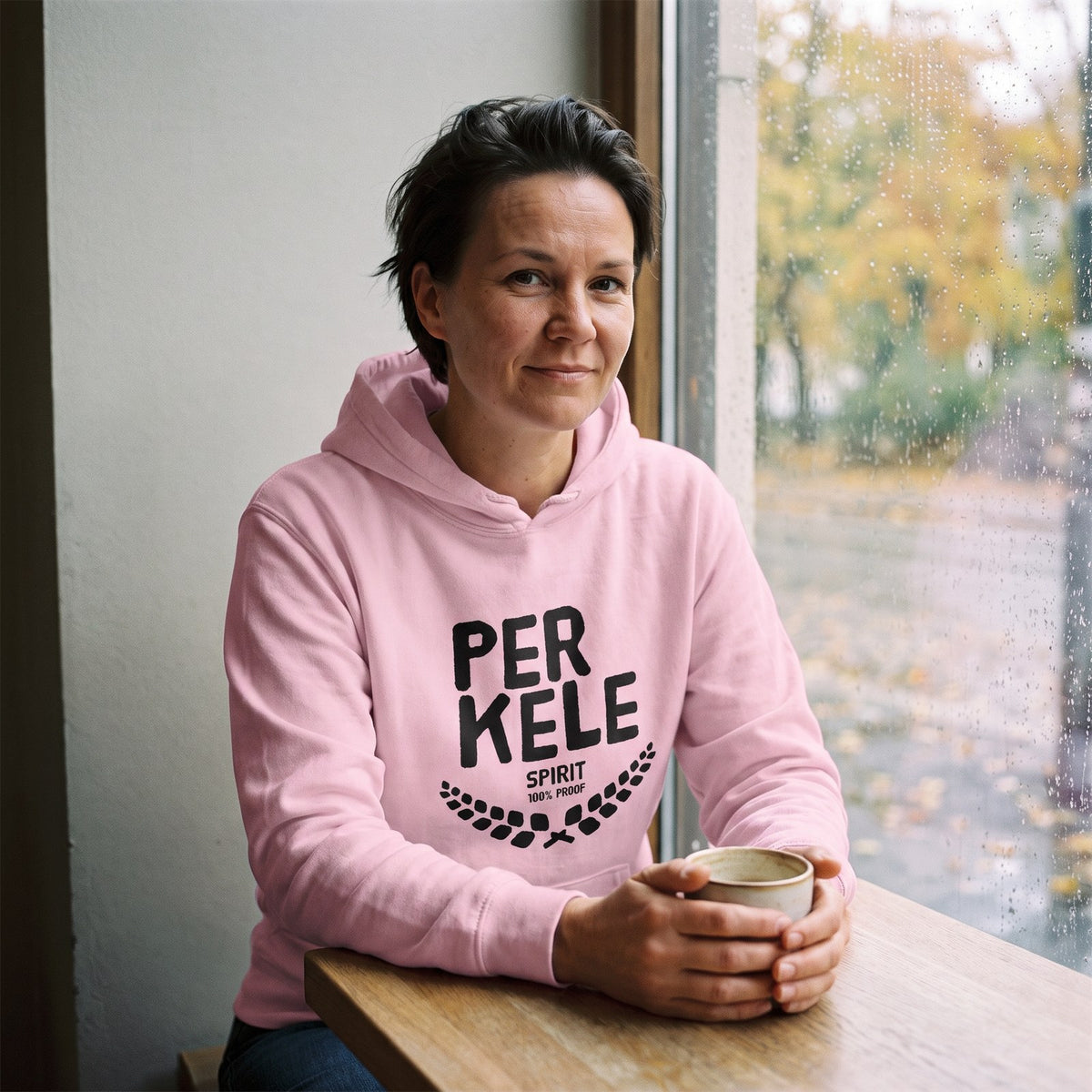 Perkele 100% Proof hoodie in light pink, worn by Katja in a Helsinki cafe window, Very Finnish Problems