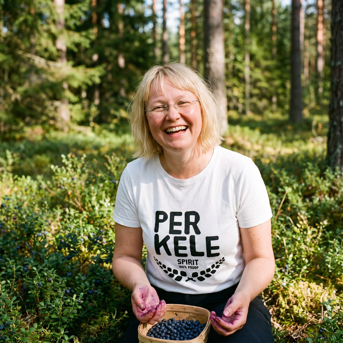 Perkele 100% Proof organic t-shirt in white, worn by Marika picking blueberries, Very Finnish Problems
