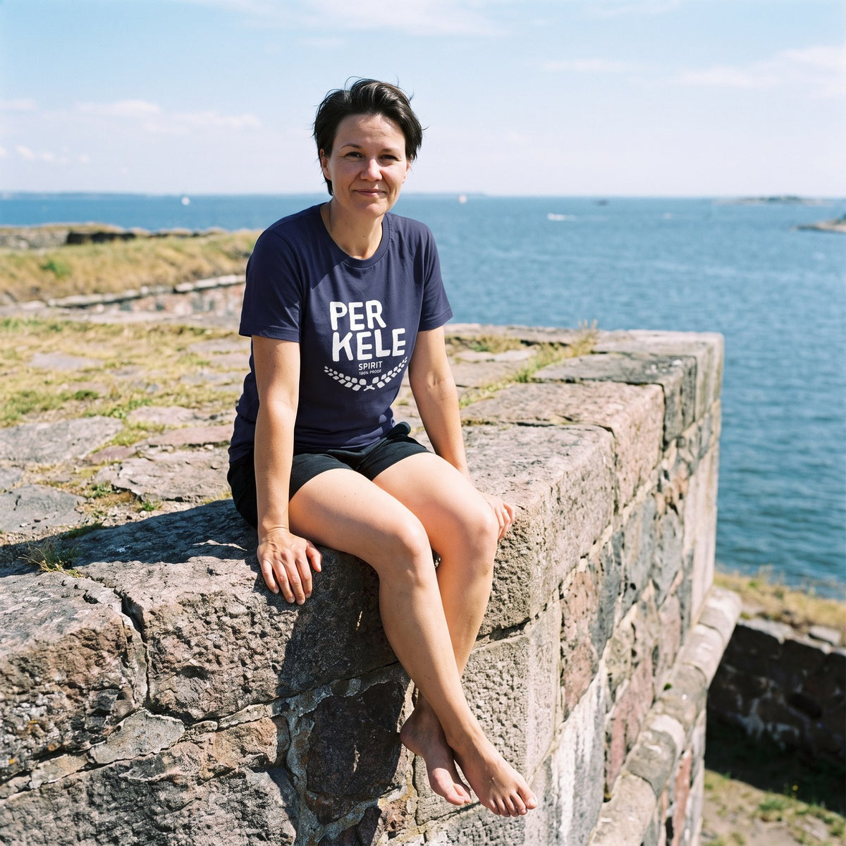 Perkele 100% Proof t-shirt in navy, worn by Katja on the Suomenlinna walls, Very Finnish Problems