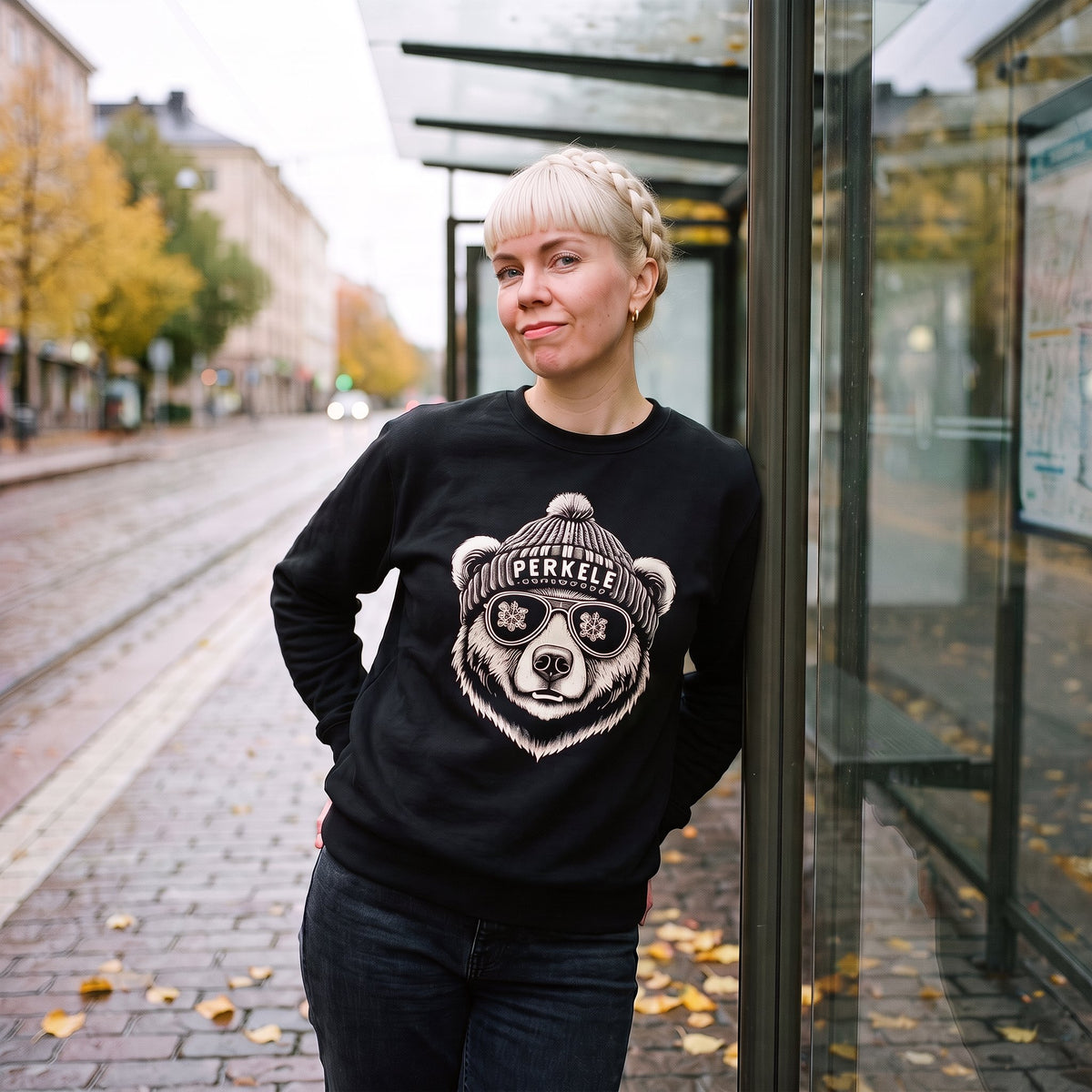 Perkele Bear sweatshirt in black, worn by Venla leaning on an autumn tram shelter in Helsinki, Very Finnish Problems