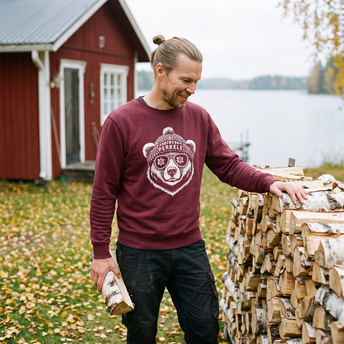 Perkele Bear sweatshirt in maroon, worn by Joonas at a woodpile beside a red summer cottage, Very Finnish Problems