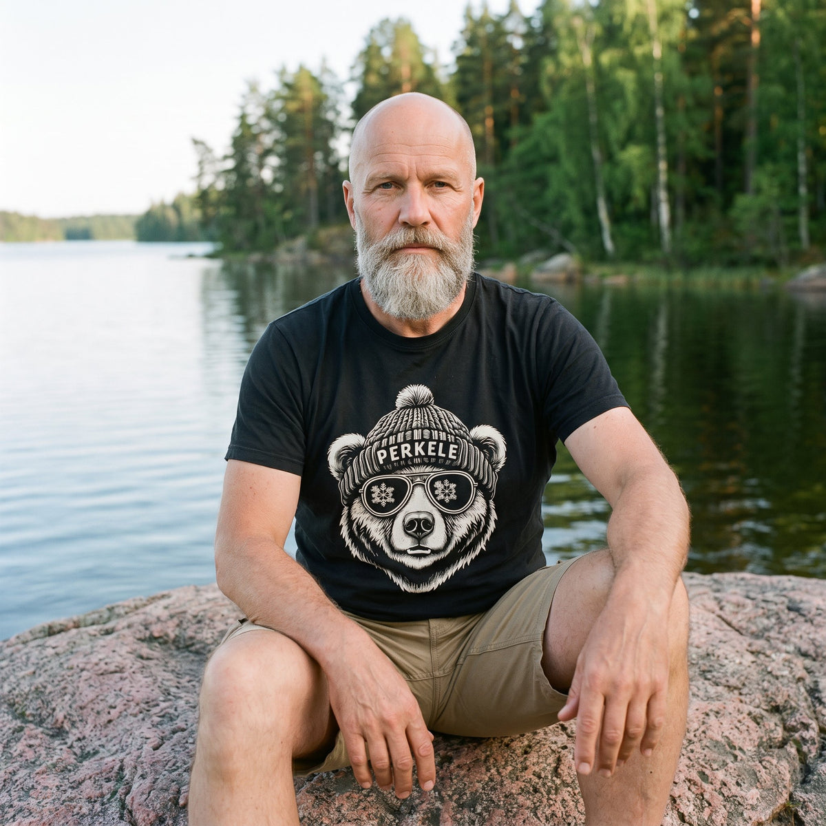 Perkele Bear t-shirt in black, worn by Mikko sitting on a lakeside rock, Very Finnish Problems