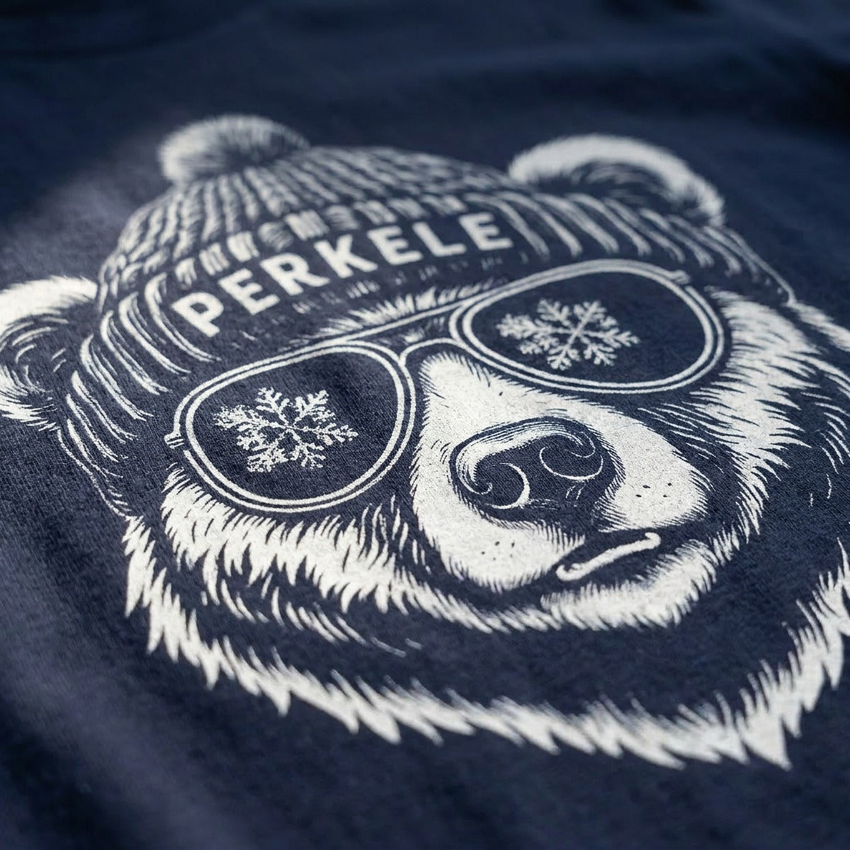 Close-up of the Perkele Bear screen print, a white bear wearing a PERKELE bobble hat and snowflake aviator sunglasses, Very Finnish Problems