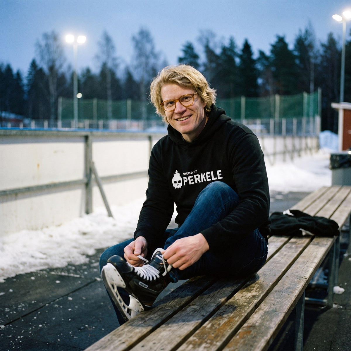 Powered by Perkele hoodie in black, worn by Tuomas lacing skates at an ice rink, Very Finnish Problems