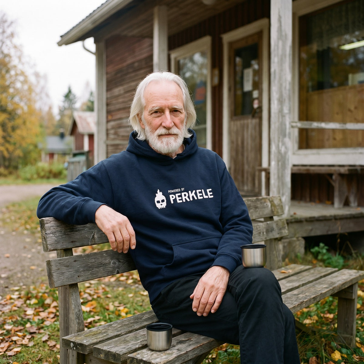 Powered by Perkele hoodie in navy, worn by Pertti outside a village shop, Very Finnish Problems