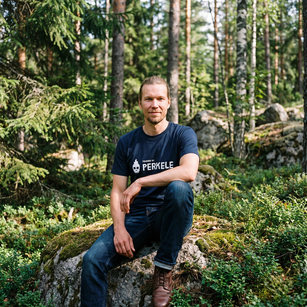 Powered by Perkele organic t-shirt in french navy, worn by Joonas on a forest boulder, Very Finnish Problems