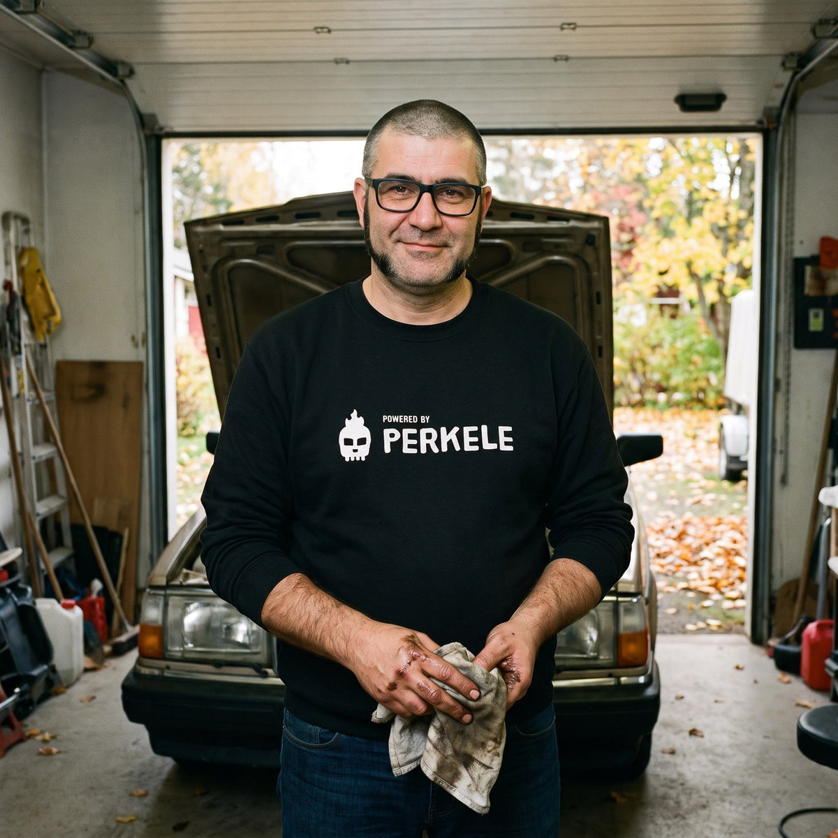Powered by Perkele sweatshirt in black, worn by Jaska in a garage workshop, Very Finnish Problems