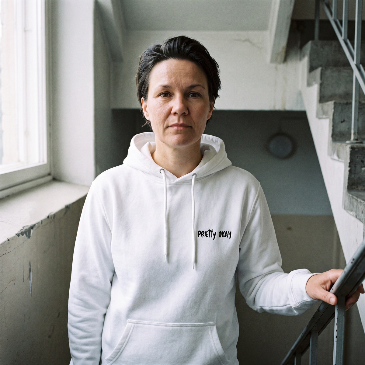 Pretty okay embroidered Finnish humour hoodie in white, worn by Katja on a stairwell landing, Very Finnish Problems