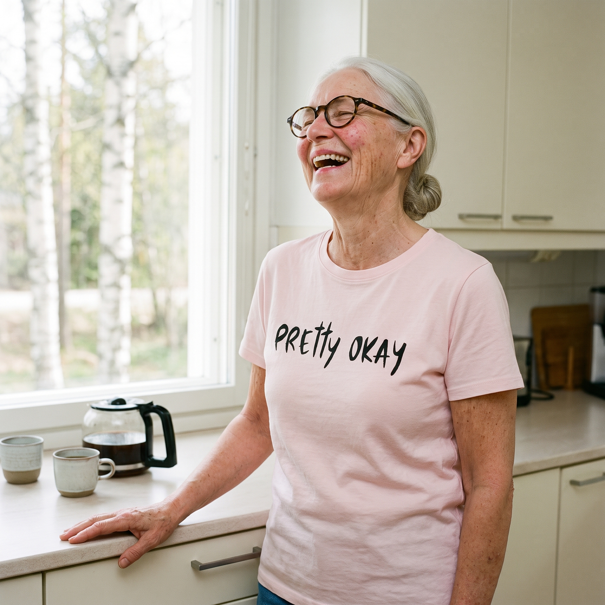 Pretty Okay t-shirt in pink, worn by a woman laughing in a kitchen, Very Finnish Problems