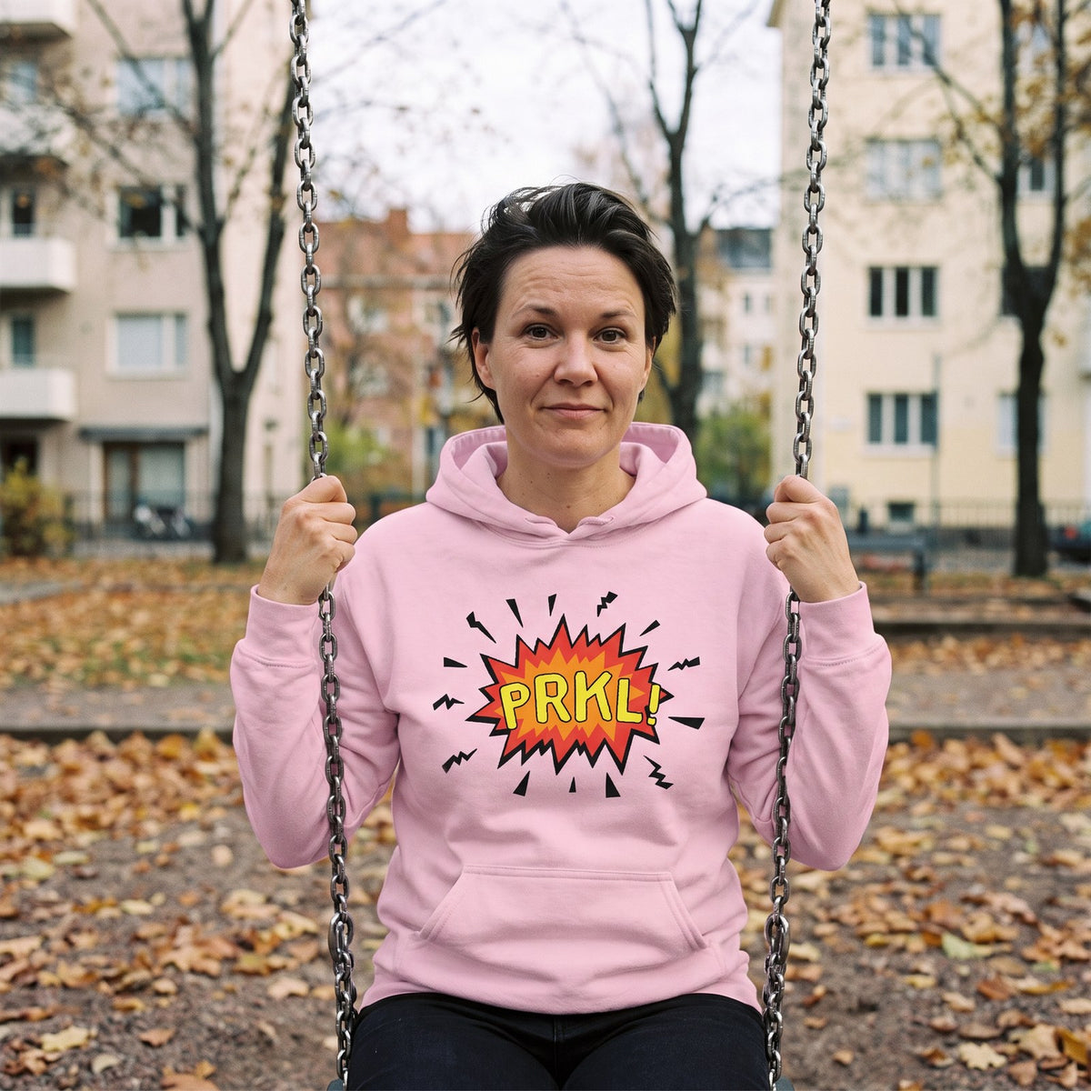 PRKL Bang hoodie in light pink, worn by Katja on a playground swing, Very Finnish Problems