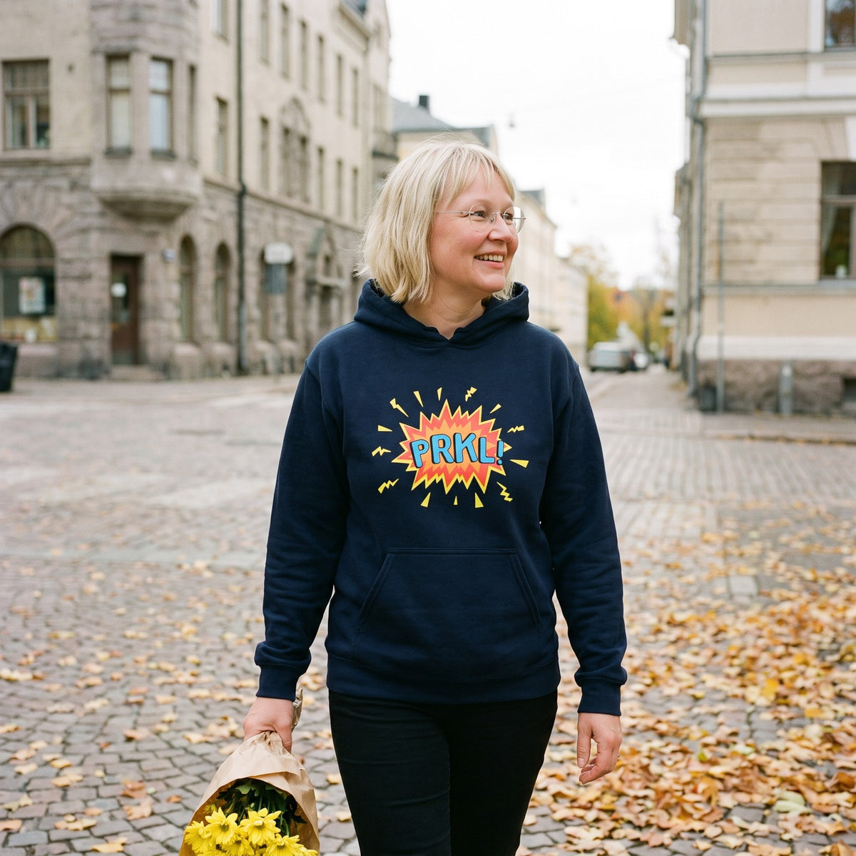 PRKL Bang hoodie in navy, worn by Marika with flowers on a town square, Very Finnish Problems
