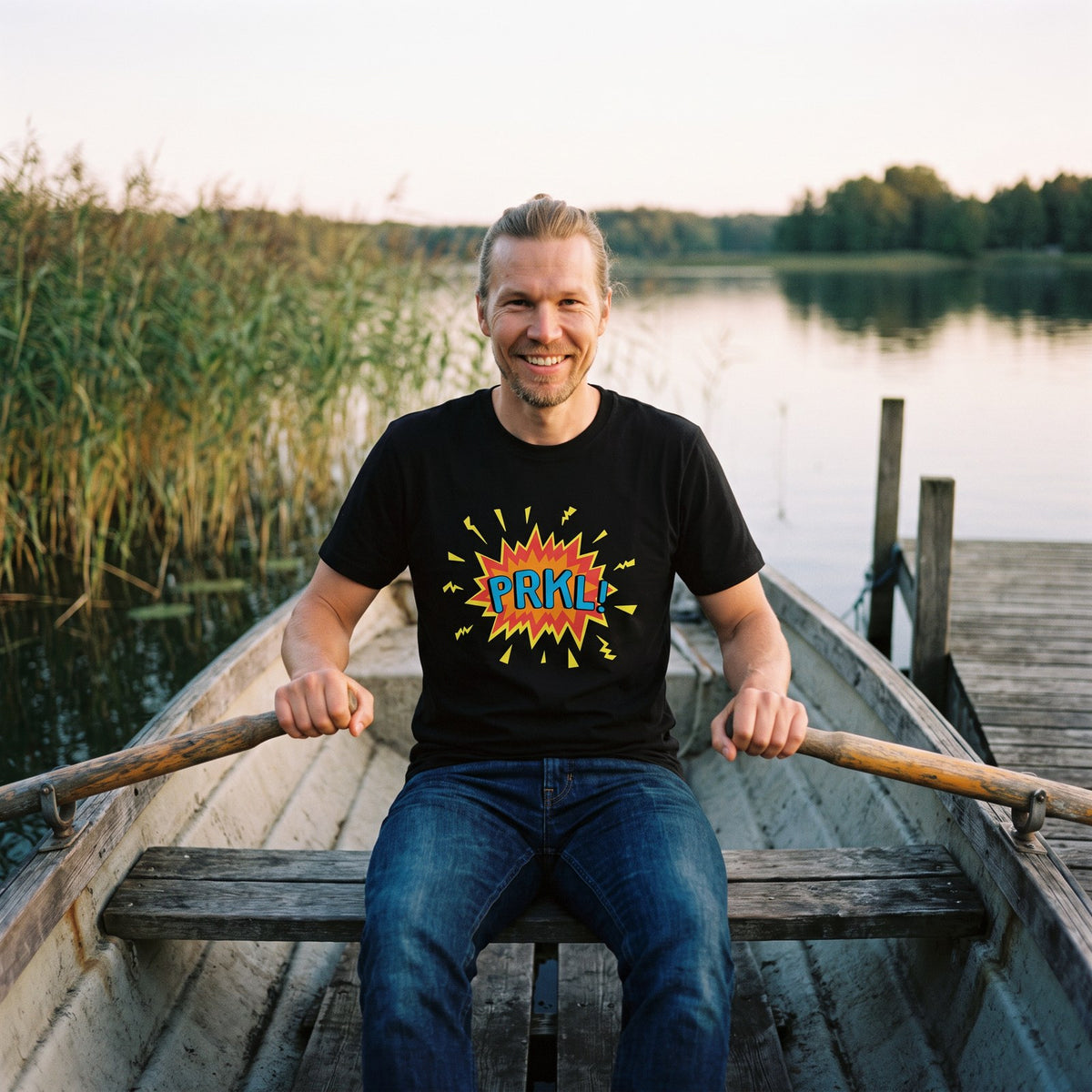 PRKL Bang organic t-shirt in black, worn by Joonas in a moored rowing boat, Very Finnish Problems