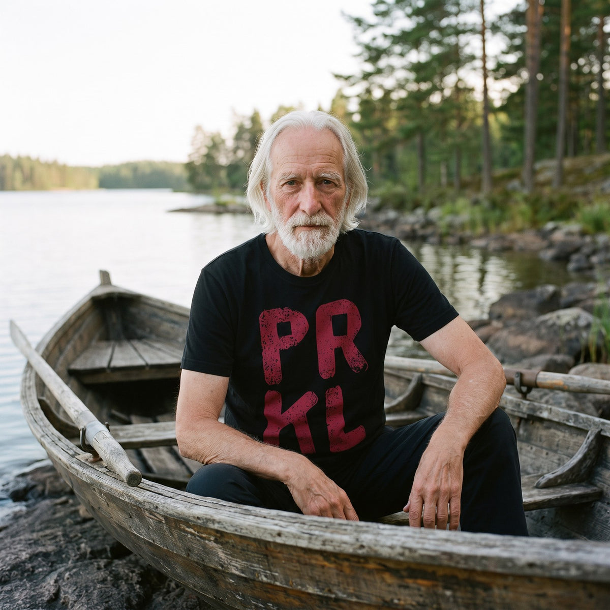 PRKL organic t-shirt in black, worn by Pertti in a lakeside rowing boat, Very Finnish Problems