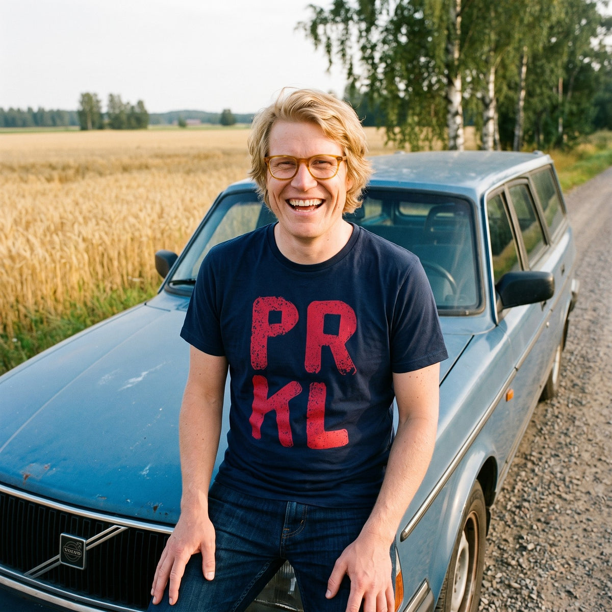 PRKL organic t-shirt in french navy, worn by Tuomas on an old Volvo by a wheat field, Very Finnish Problems