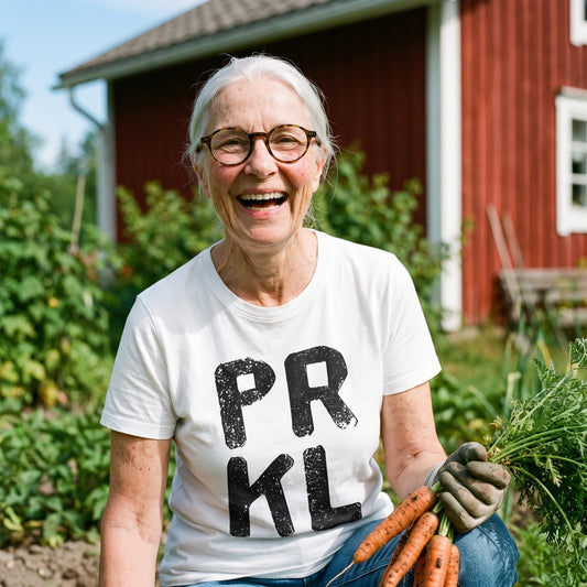 PRKL organic t-shirt in white, worn by Raija in a cottage vegetable garden, Very Finnish Problems