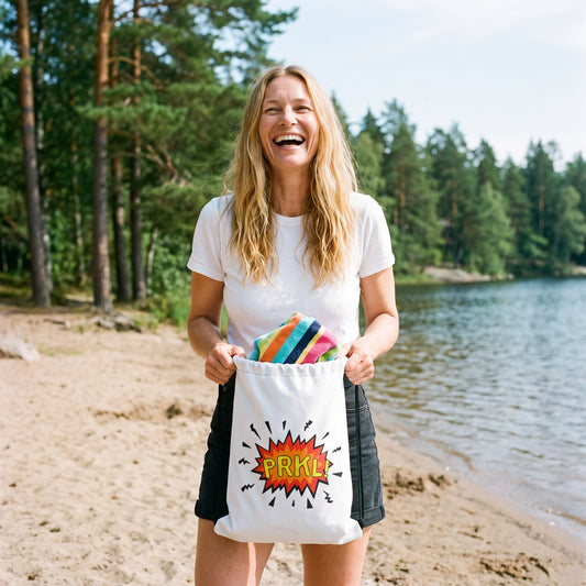 PRKL and PRKL Bang drawstring bag, held by Elina on a lake beach, PRKL Bang side, Very Finnish Problems