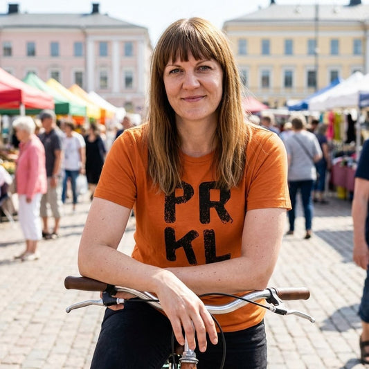 PRKL Finnish language t-shirt in burnt orange, worn with a bicycle on a market square, Very Finnish Problems