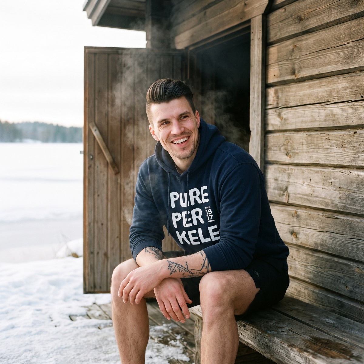 Pure Perkele since 1917 hoodie in navy, worn by Eetu outside a lakeside smoke sauna, Very Finnish Problems