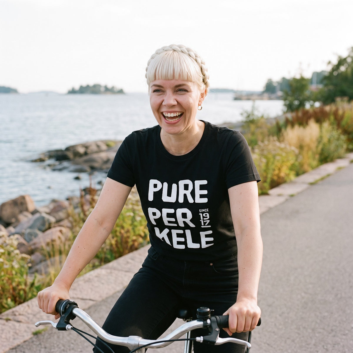 Pure Perkele since 1917 organic t-shirt in black, worn by Venla cycling on the Helsinki seafront, Very Finnish Problems