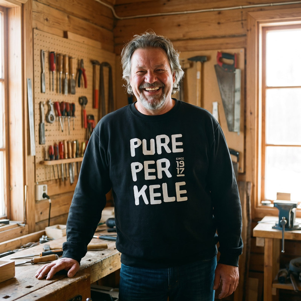 Pure Perkele since 1917 sweatshirt in black, worn by Jojelli grinning in a wooden workshop, Very Finnish Problems
