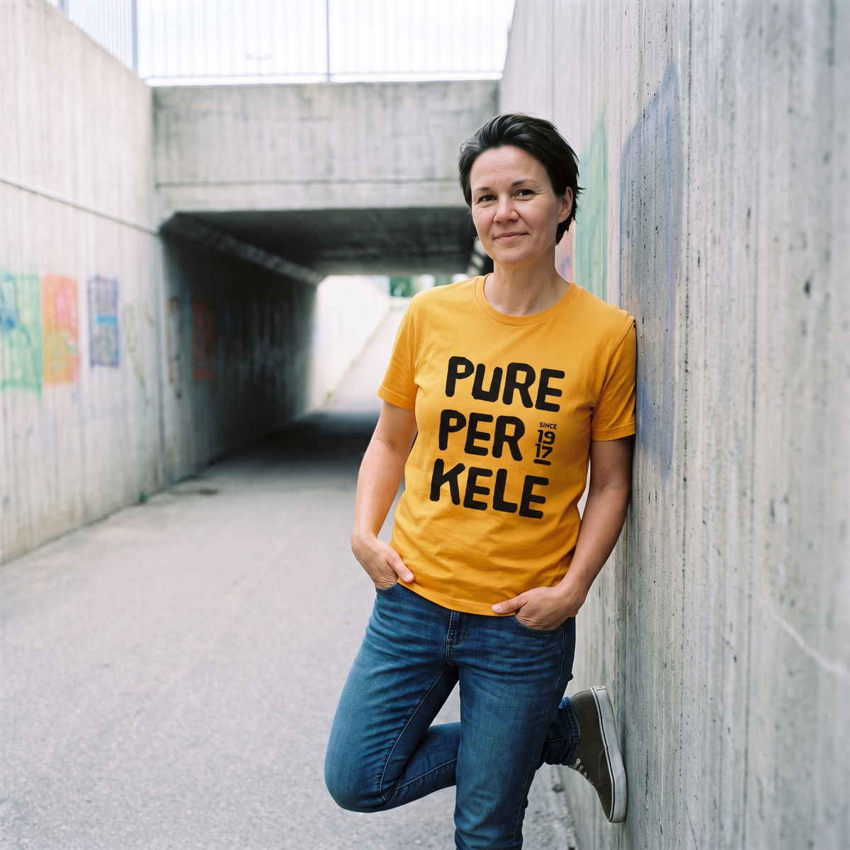 Pure Perkele since 1917 t-shirt in gold, worn by Katja in a painted underpass, Very Finnish Problems