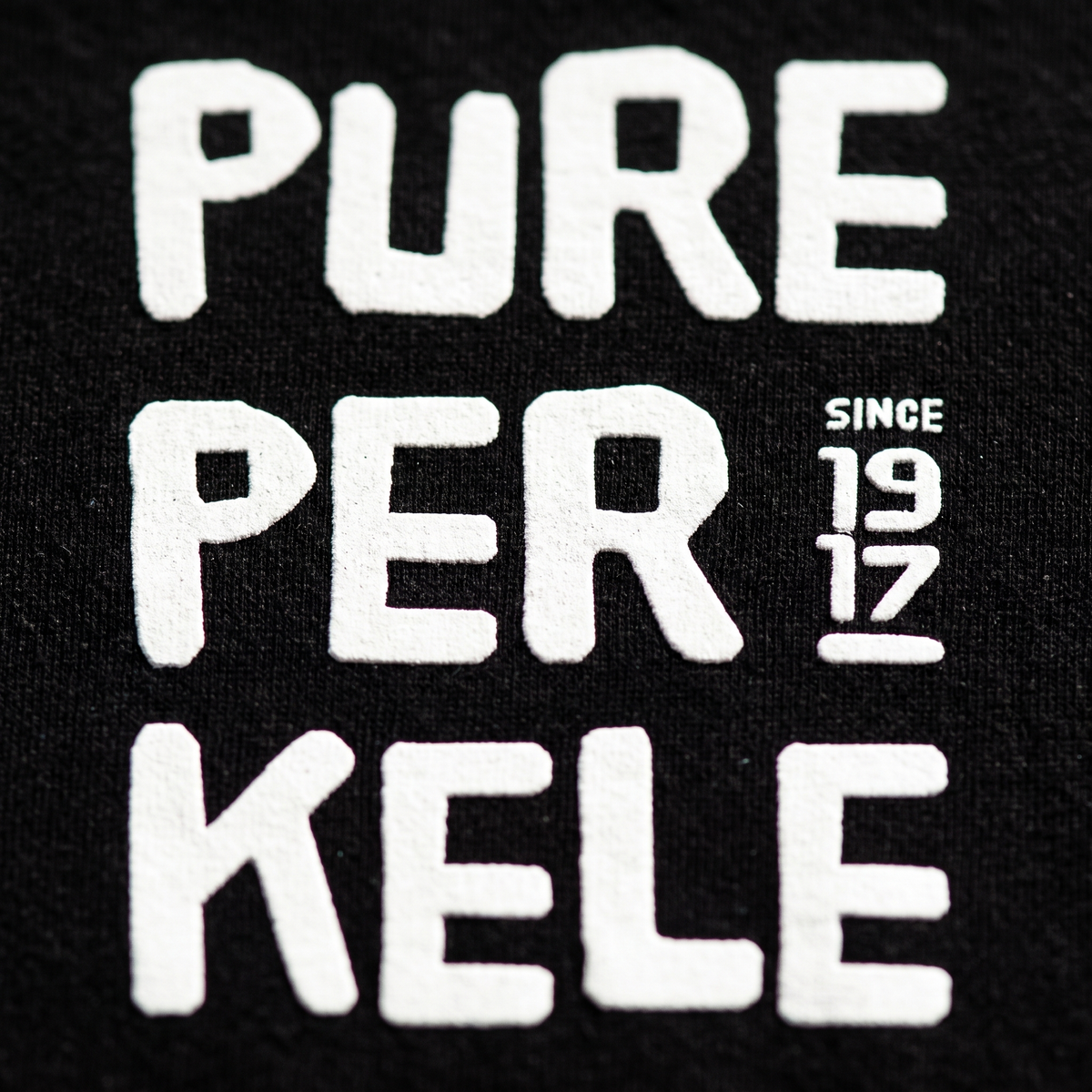 Close-up of the Pure Perkele since 1917 print on black t-shirt fabric, Very Finnish Problems