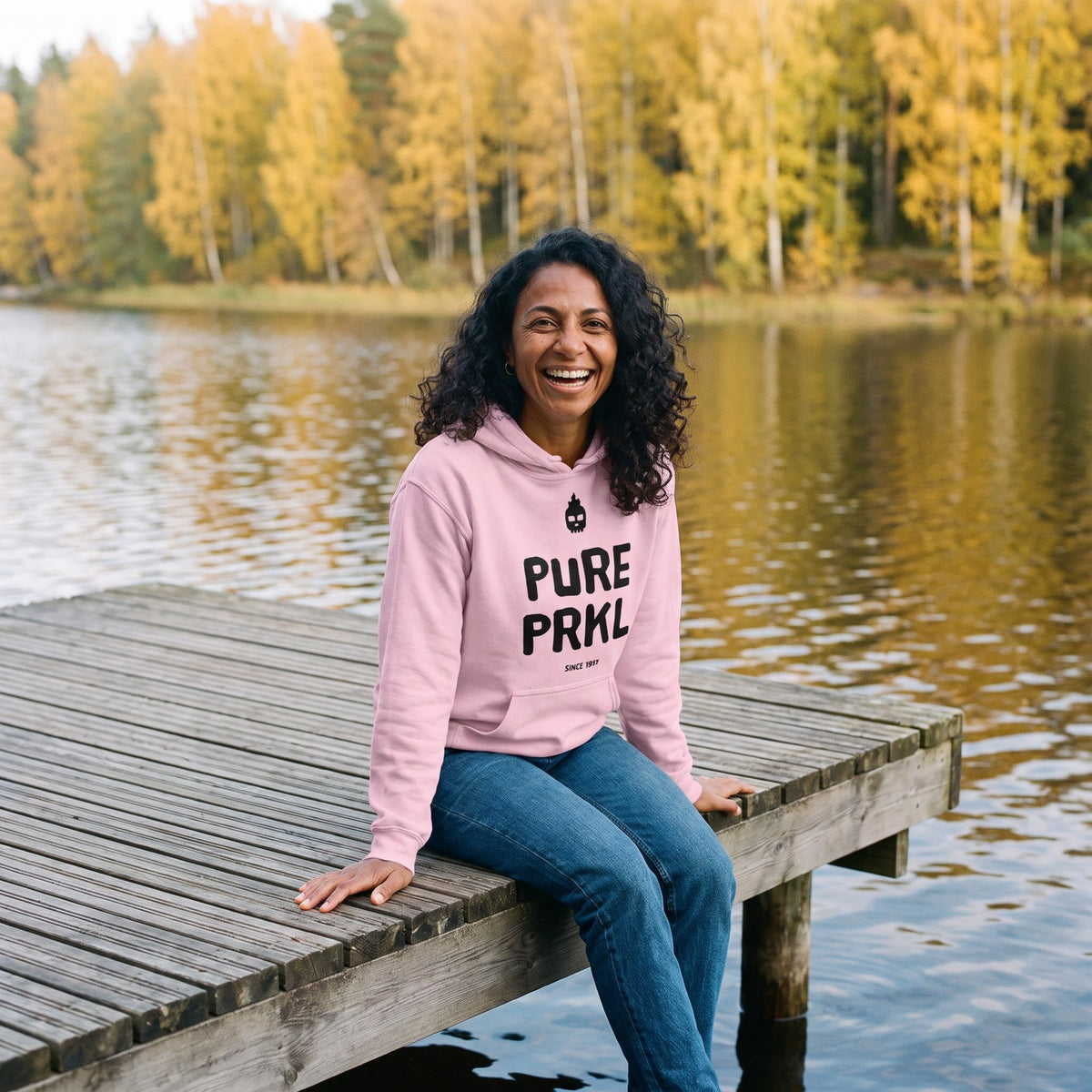 Pure PRKL hoodie in light pink, worn by Nea on a lake pier, Very Finnish Problems