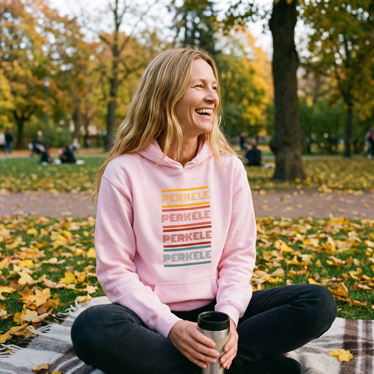 Retro Perkele hoodie in light pink, worn by Elina picnicking in a Helsinki park, Very Finnish Problems