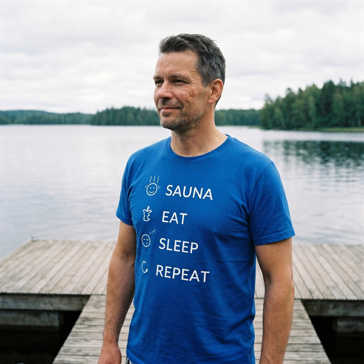 Man on a lakeside sauna jetty wearing the blue Sauna Eat Sleep Repeat t-shirt, Very Finnish Problems