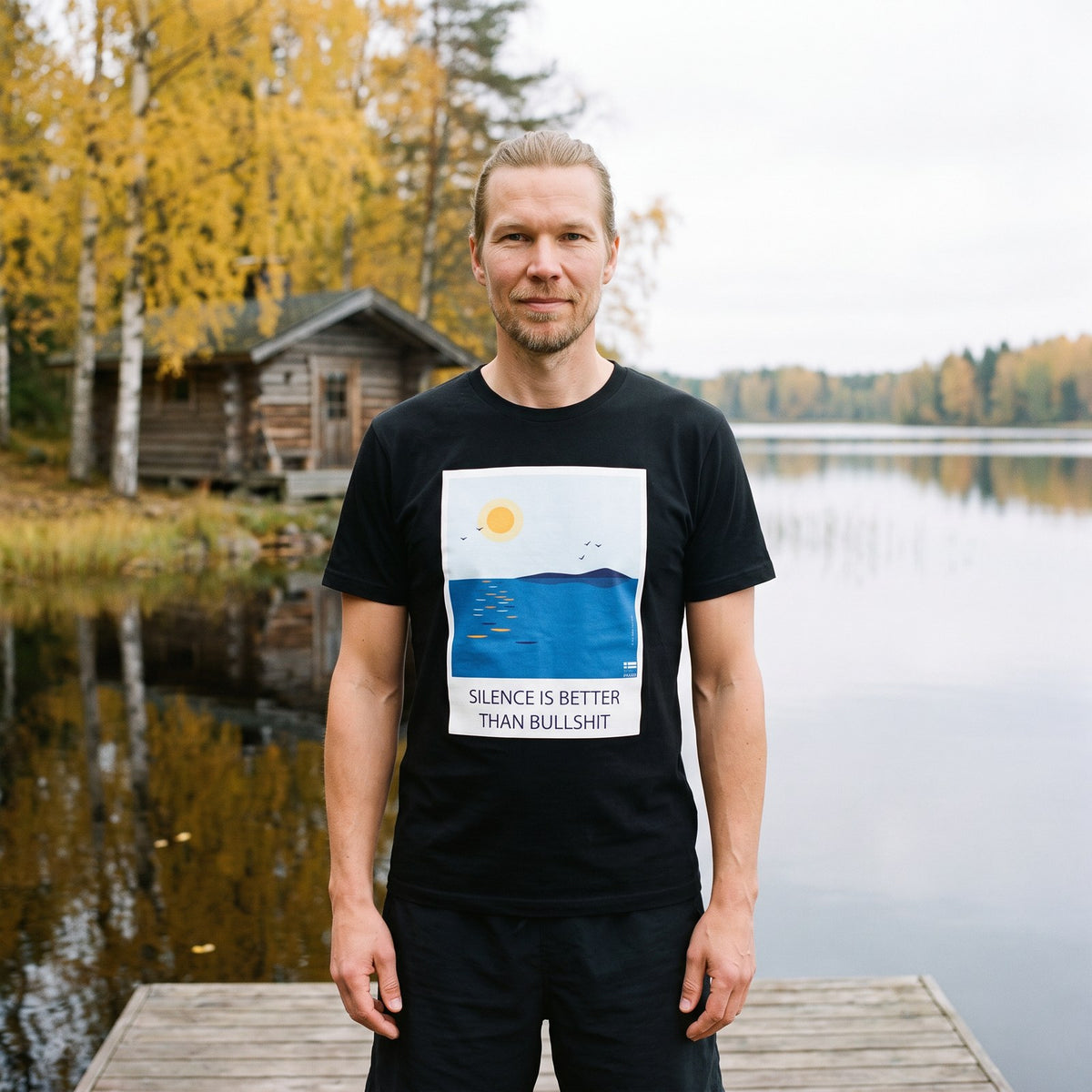 Silence Is Better Than Bullshit organic t-shirt in black, worn by Joonas on a lakeside sauna dock, Very Finnish Problems