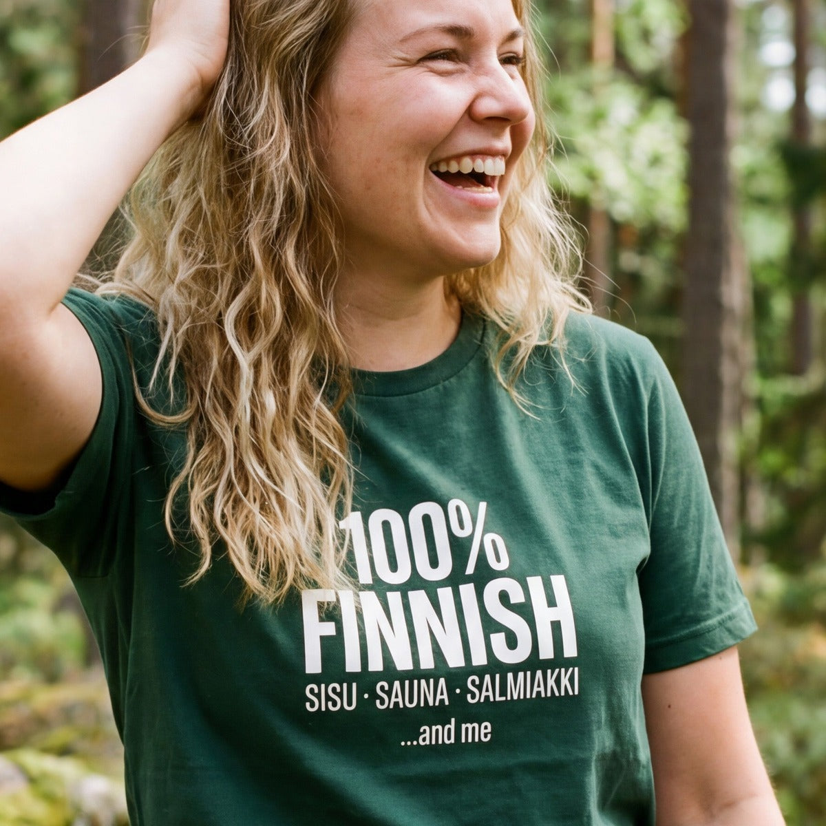 Woman laughing in a Finnish forest wearing the 100% Finnish Sisu Sauna Salmiakki t-shirt in forest green