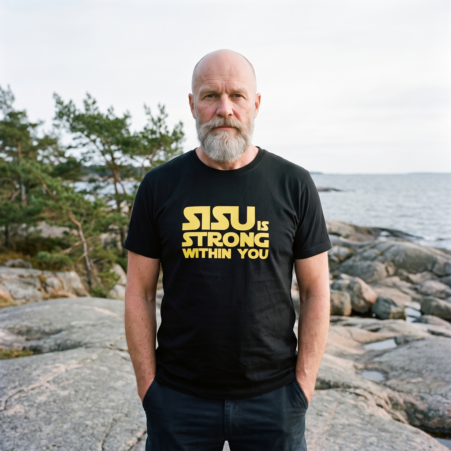 Sisu is Strong organic cotton t-shirt in black, worn by a man on a granite Baltic shore, Very Finnish Problems