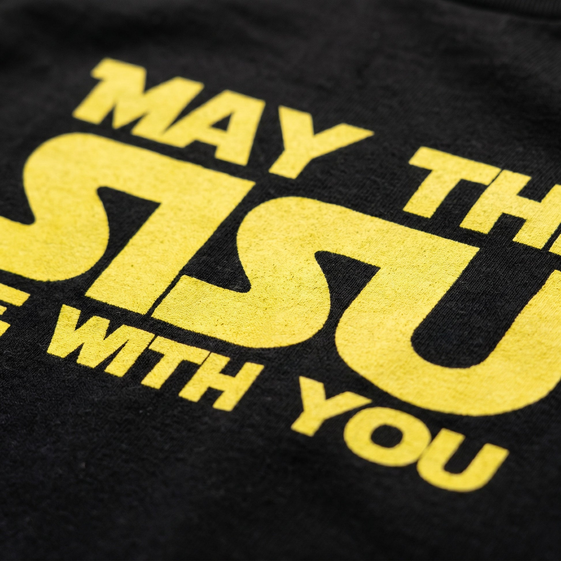 Close-up of the yellow May the Sisu Be With You screen print on a black t-shirt, Very Finnish Problems