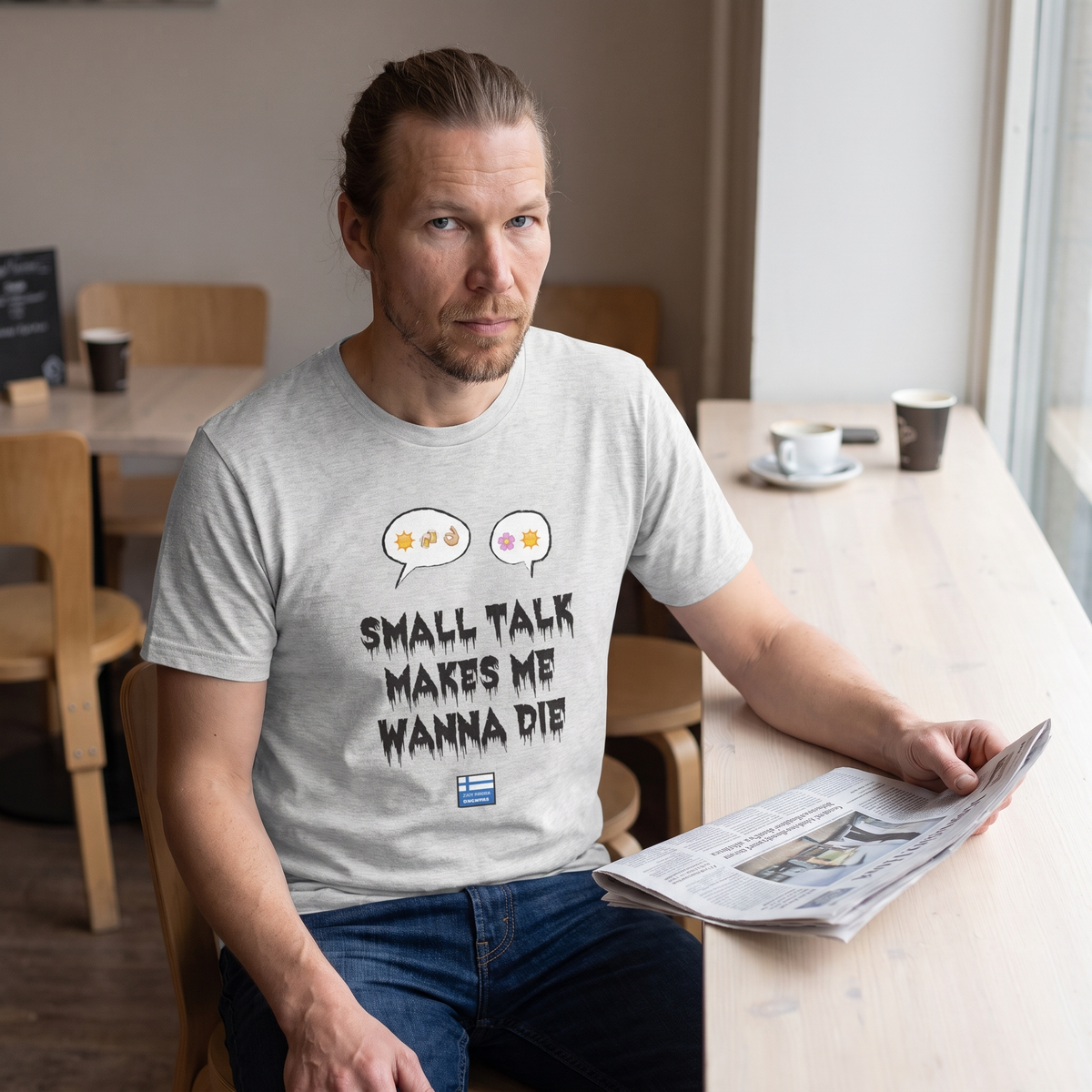 Small Talk Makes Me Wanna Die t-shirt in grey, worn by Joonas warily at a cafe table, Very Finnish Problems