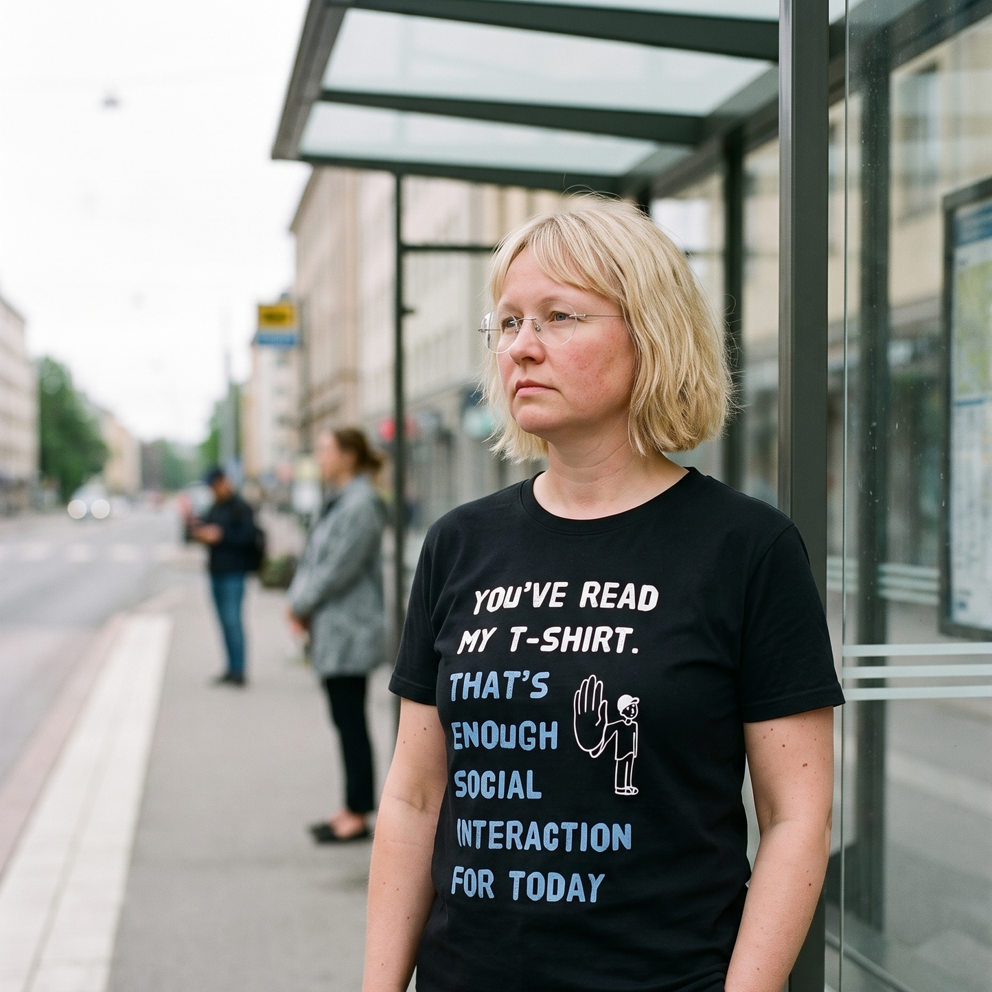 Social Interaction t-shirt in black, worn by Marika waiting at a Helsinki bus stop, Very Finnish Problems