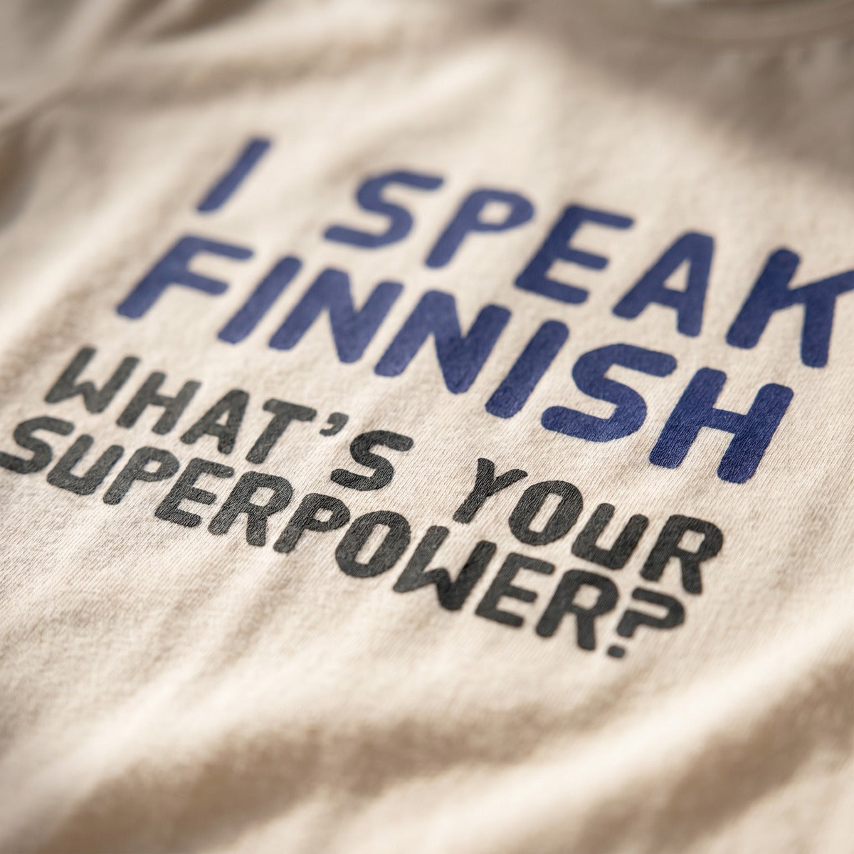 Close-up of the I Speak Finnish What's Your Superpower print on a soft cream t-shirt, Very Finnish Problems