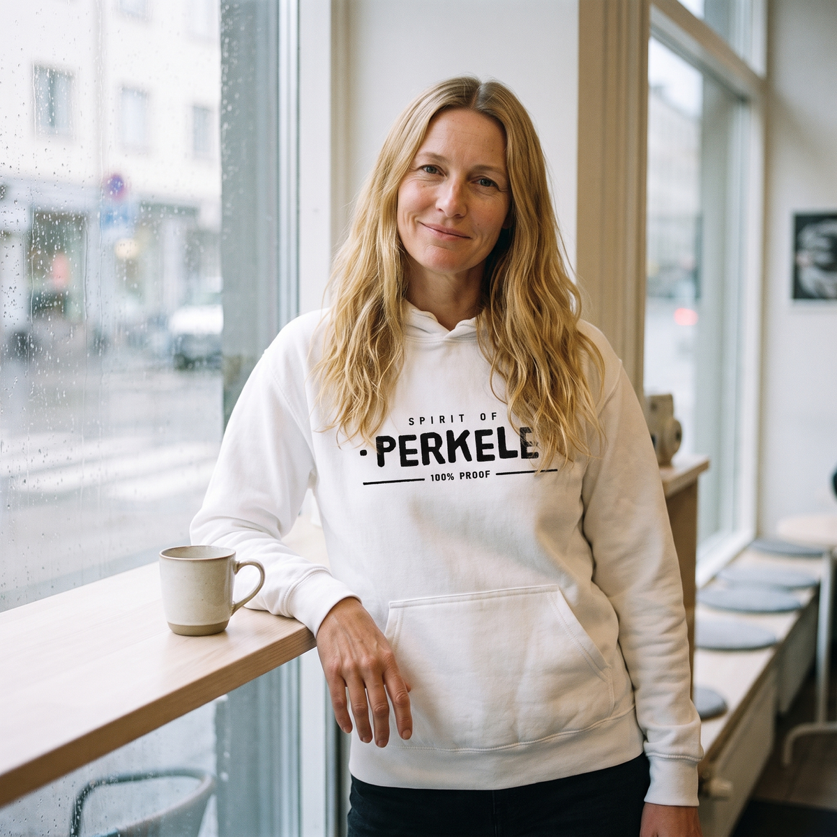 Spirit of Perkele hoodie in white, worn by Elina at a cafe window with a coffee, Very Finnish Problems
