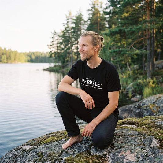 Spirit of Perkele organic t-shirt in black, worn by Joonas on a lakeside rock, Very Finnish Problems