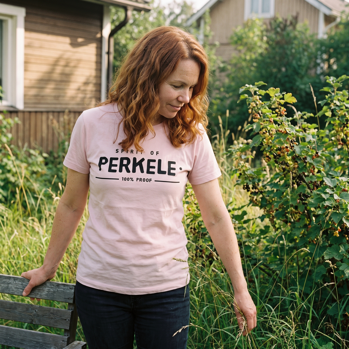 Spirit of Perkele t-shirt in pink, worn by a woman in a summer garden, Very Finnish Problems