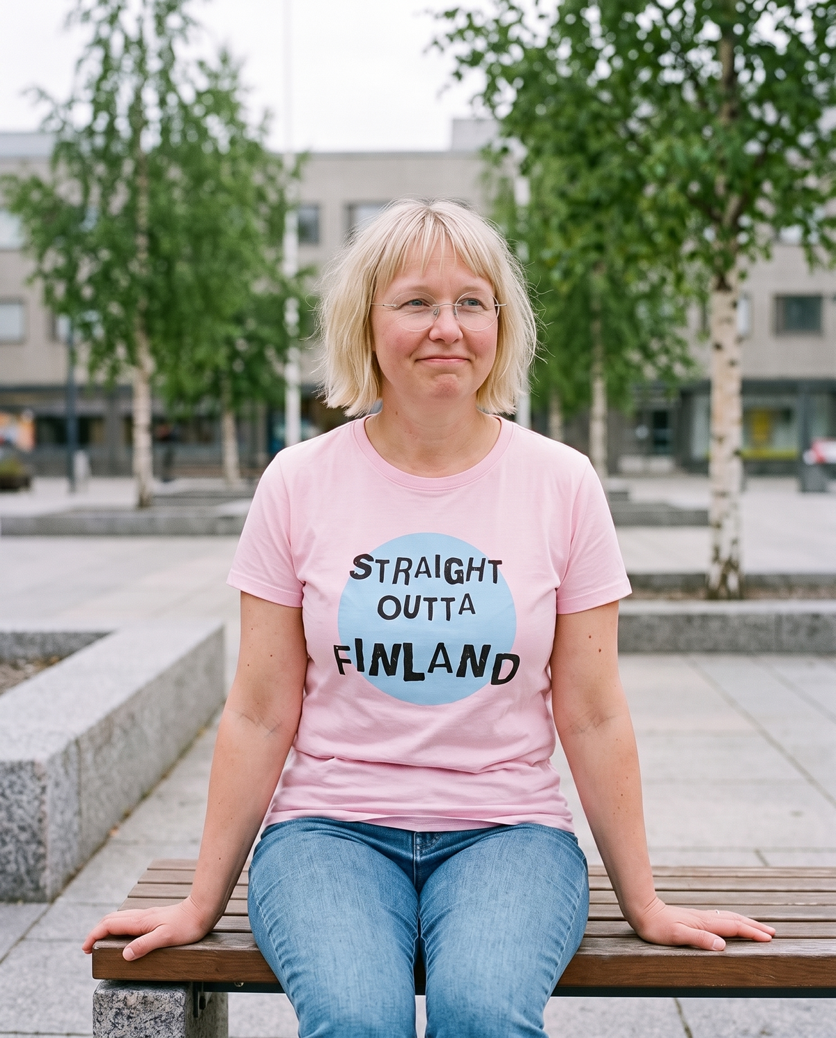 Straight Outta Finland t-shirt in pink, worn by Marika on a bench in a Finnish city plaza, Very Finnish Problems